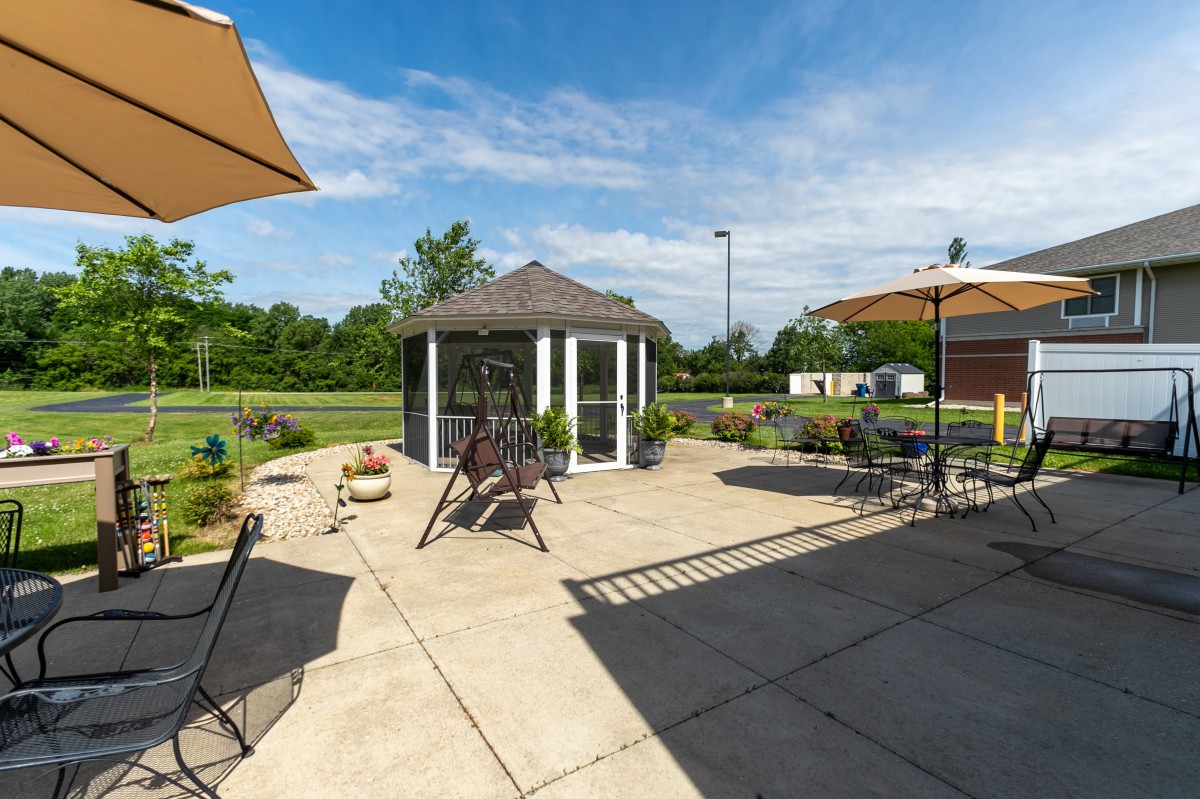 A spacious outdoor patio featuring a gazebo and several umbrellas, surrounded by greenery on a sunny day.