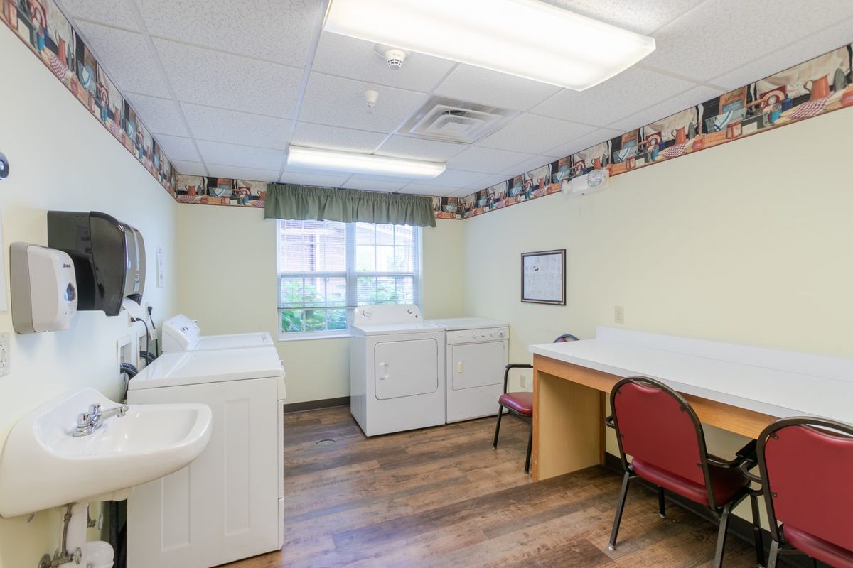 A well-lit laundry room with two washing machines, a dryer, a folding table, and a chair.