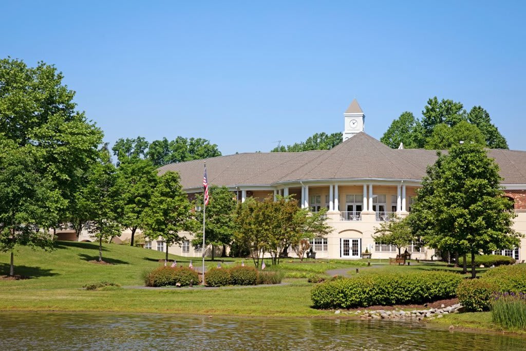 A scenic view of a large building surrounded by trees with a small lake in the foreground.