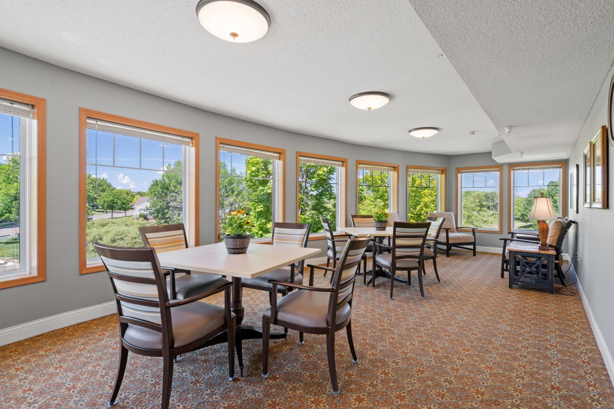 A bright dining area with multiple tables and chairs, surrounded by large windows letting in natural light.
