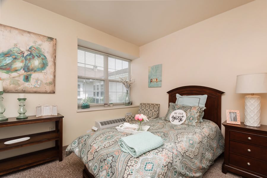 A cozy bedroom with a single bed, decorative pillows, and a large window.