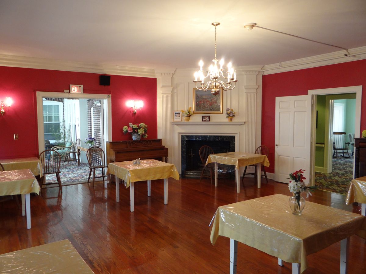 A cozy dining room with red walls, wooden floors, and yellow tablecloths.