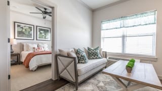 A cozy living room with a sofa, decorative pillows, and a view into the adjacent bedroom.