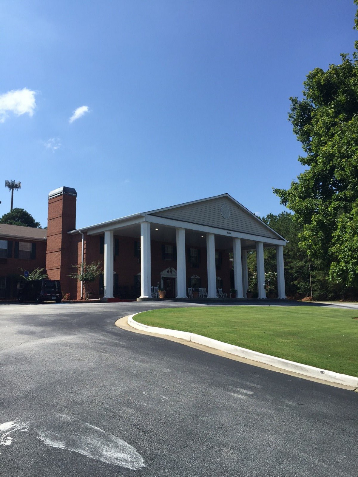 A brick building with large white columns and a driveway under a clear blue sky.