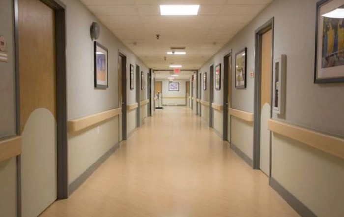 A sterile, empty hospital hallway with closed doors and fluorescent lighting.