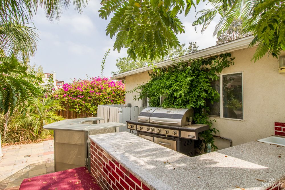 A cozy outdoor patio with a barbecue grill surrounded by lush greenery and colorful flowers.