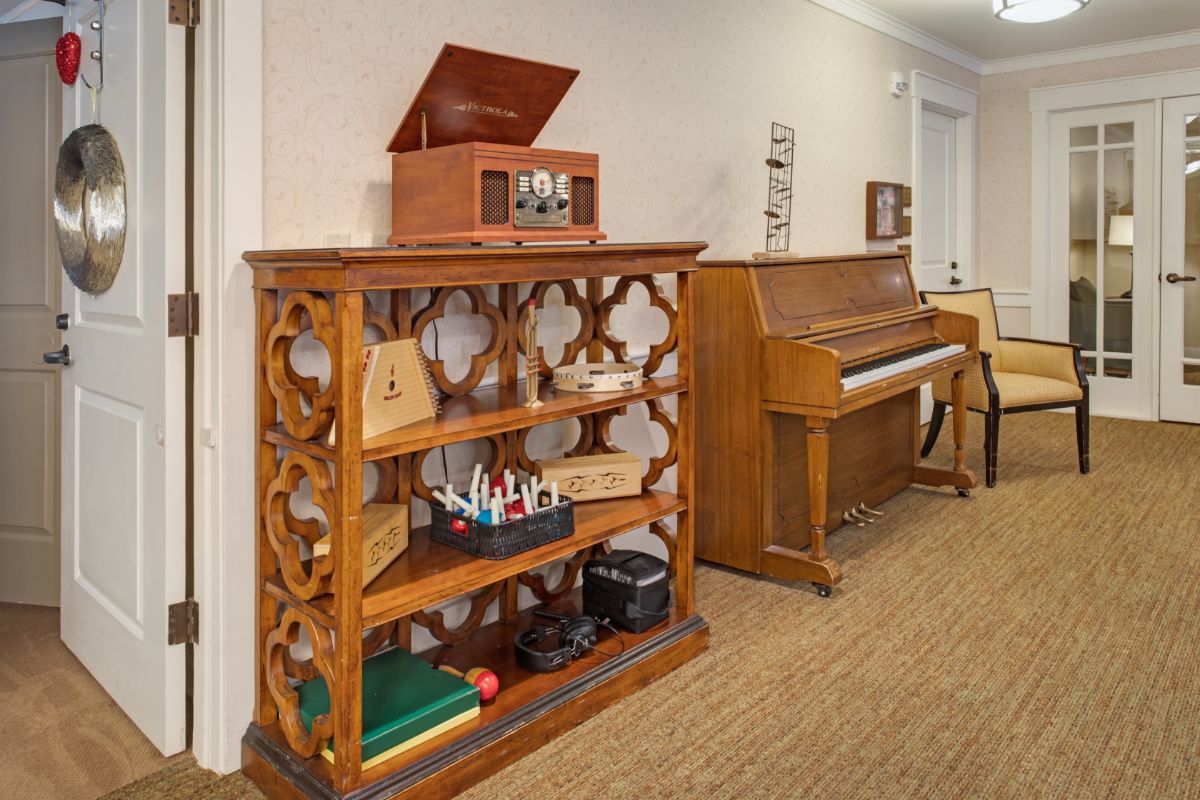 A cozy room featuring a decorative bookshelf with a record player on top and a piano in the background.
