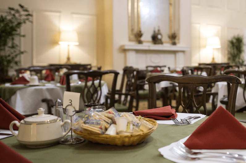 An elegant restaurant dining room featuring neatly set tables with baskets of bread and colorful napkins.