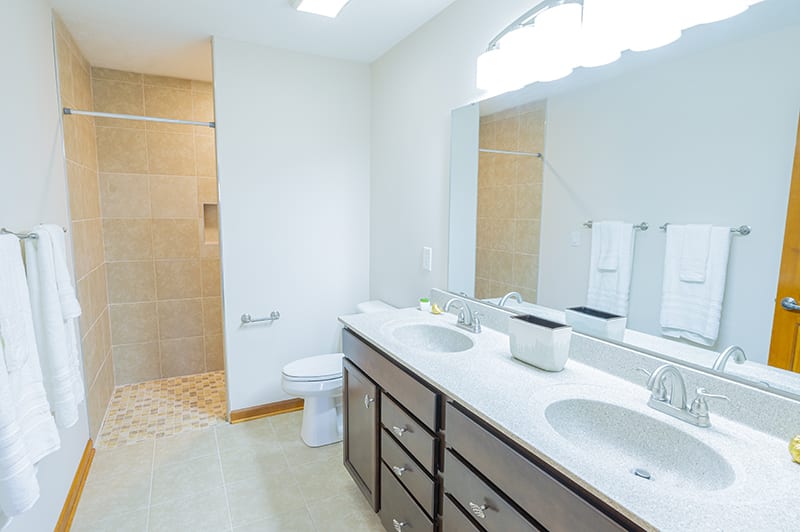 A modern bathroom with double sinks, a large mirror, and a glass-enclosed shower.