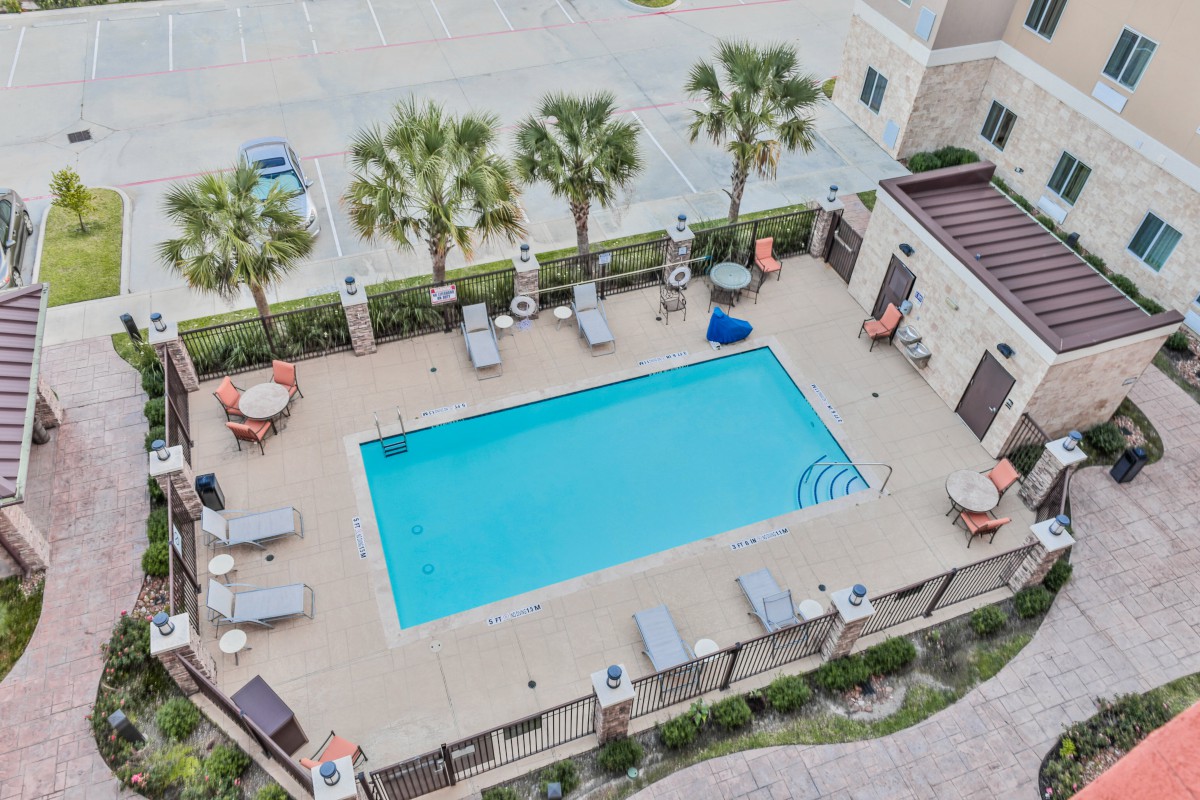 An aerial view of an outdoor swimming pool surrounded by lounge chairs and palm trees.