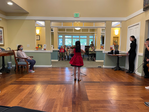 A young girl performs on stage in a red dress while an audience looks on, showcasing talent and joy at a community gathering.