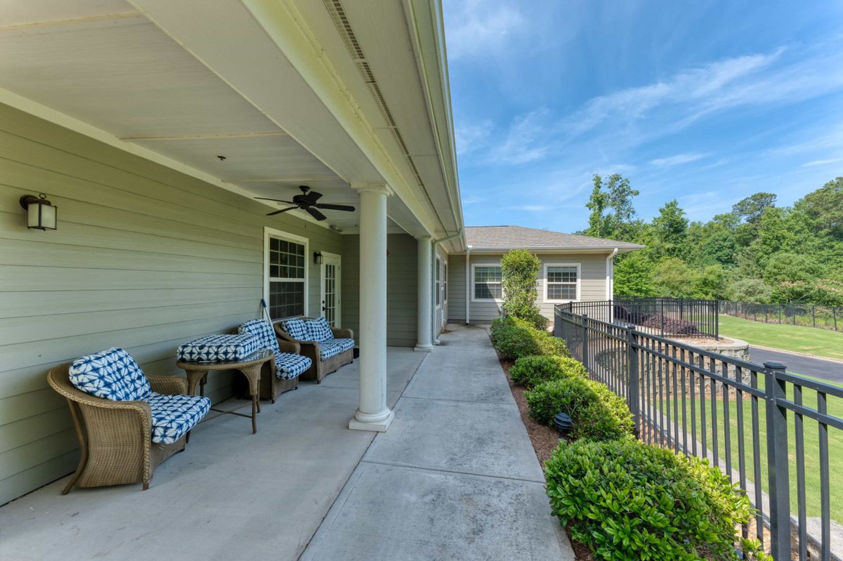 A charming covered patio with outdoor seating, surrounded by lush landscaping and a fenced garden area.