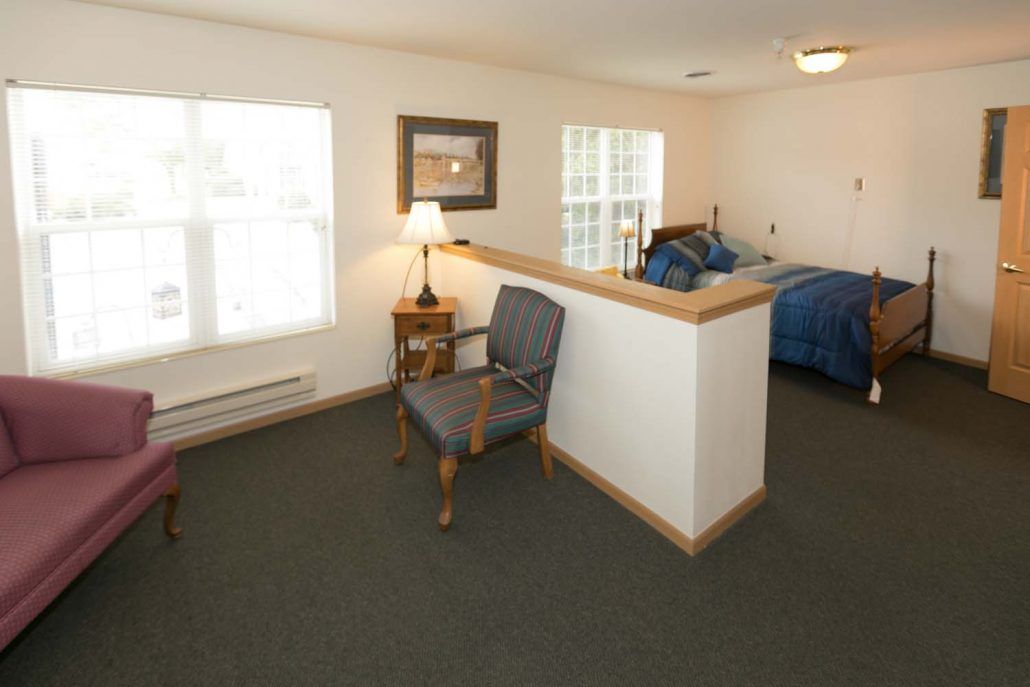 A cozy bedroom with a chair, lamp, and bed near windows.