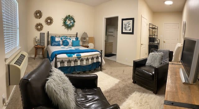 A cozy and modern bedroom with stylish decor, featuring a bed with blue and white bedding, leather armchairs, and a soft rug.