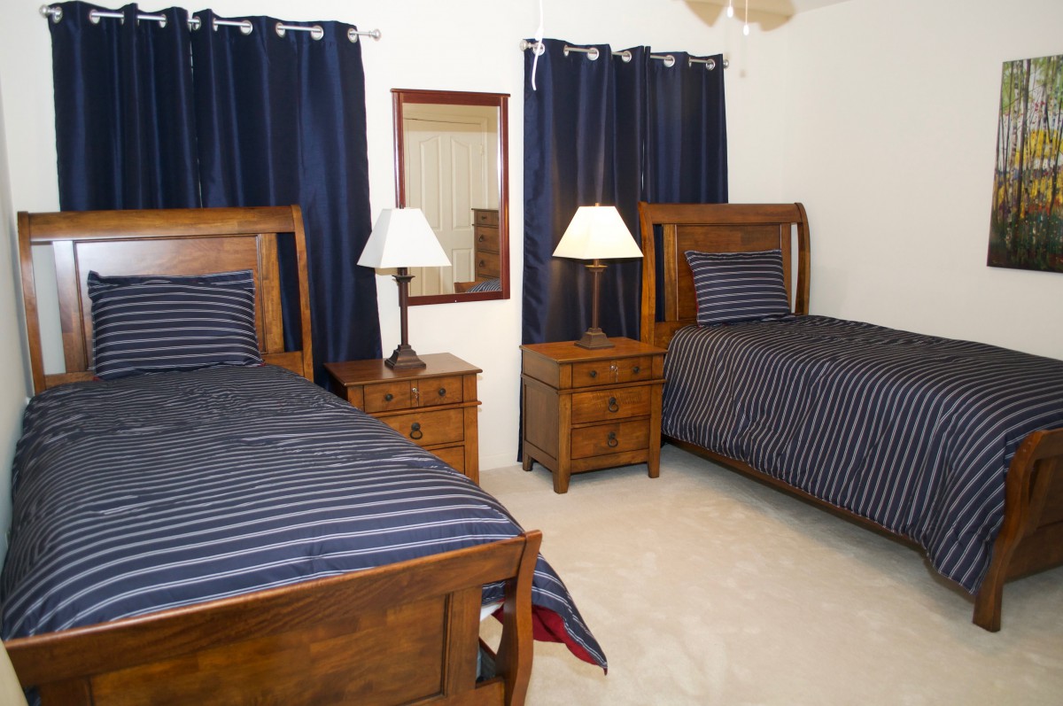 A cozy bedroom featuring two twin beds with striped bedding, wooden nightstands, and blue curtains.