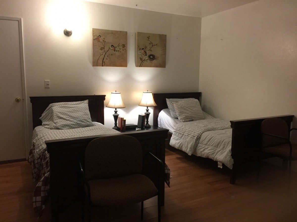 A cozy bedroom featuring two single beds, a nightstand with lamps, and artwork on the wall.