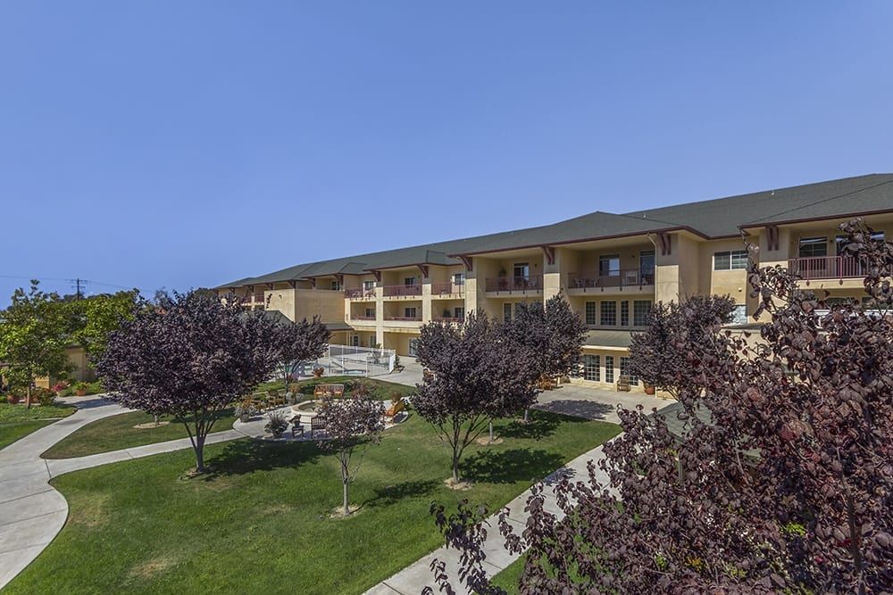 A spacious building surrounded by a well-maintained lawn and trees on a clear, sunny day.