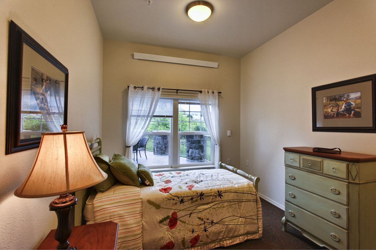 A cozy bedroom with a single bed, dresser, and lamp by the window.