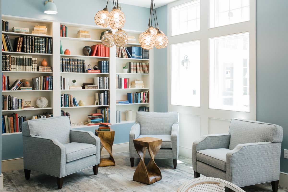 A modern living room with bookshelves, comfortable chairs, and stylish lighting.