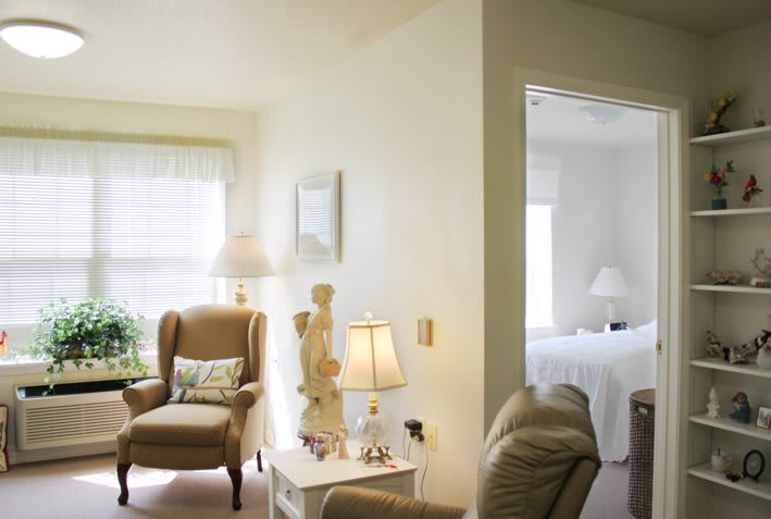 A cozy living room with comfortable seating and soft lighting, leading into a bedroom.