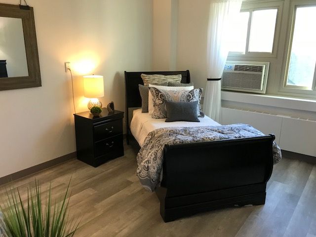 A cozy bedroom with a single bed, nightstand, and warm lighting.