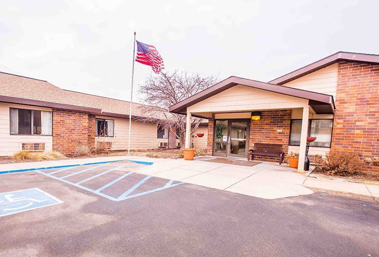 The entrance of a brick building with an American flag and designated handicap parking spaces.