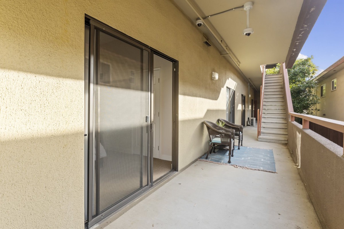 A view of an apartment corridor with a sliding door, outdoor chairs and table, and stairs in the background.