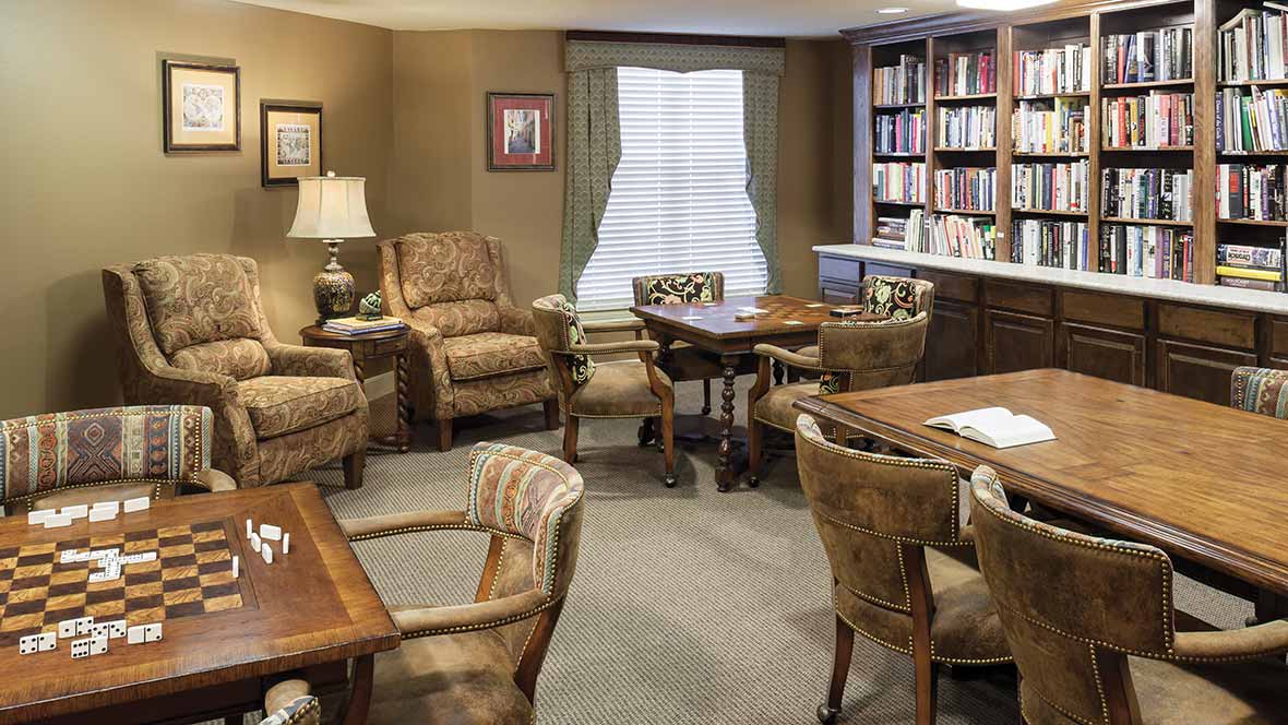 A cozy living room with comfortable chairs, wooden tables, and a well-stocked bookshelf.