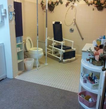 An accessible bathroom with safety equipment and a specialized chair.