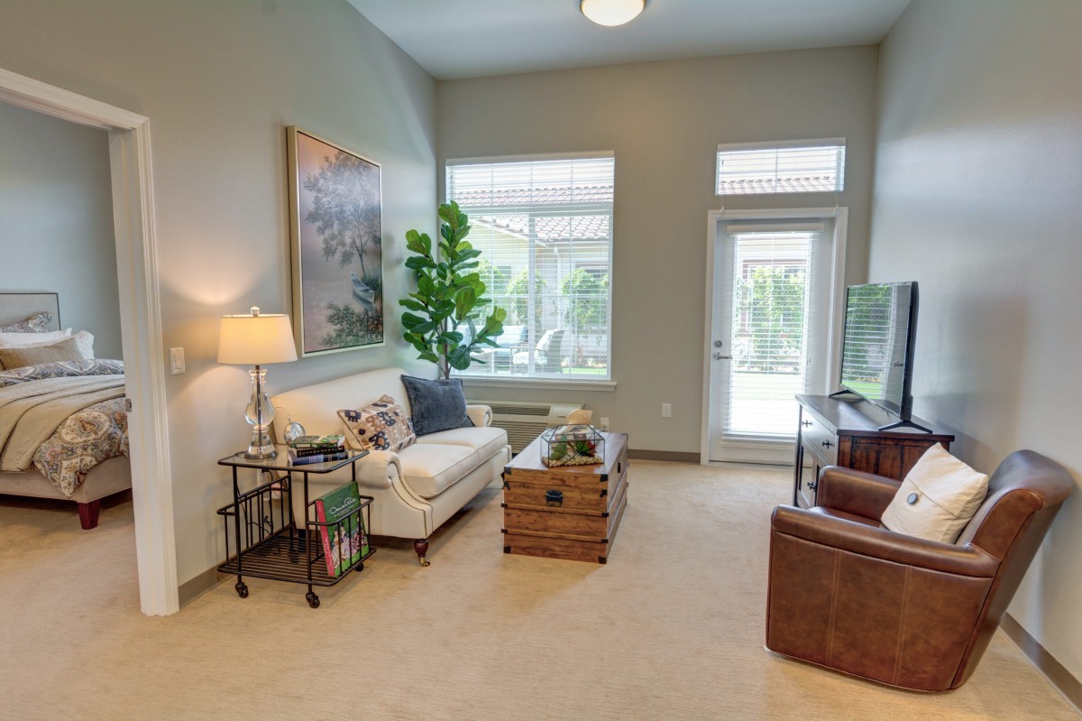 A cozy living room featuring a sofa, armchair, and a coffee table, well-lit by natural light from large windows.