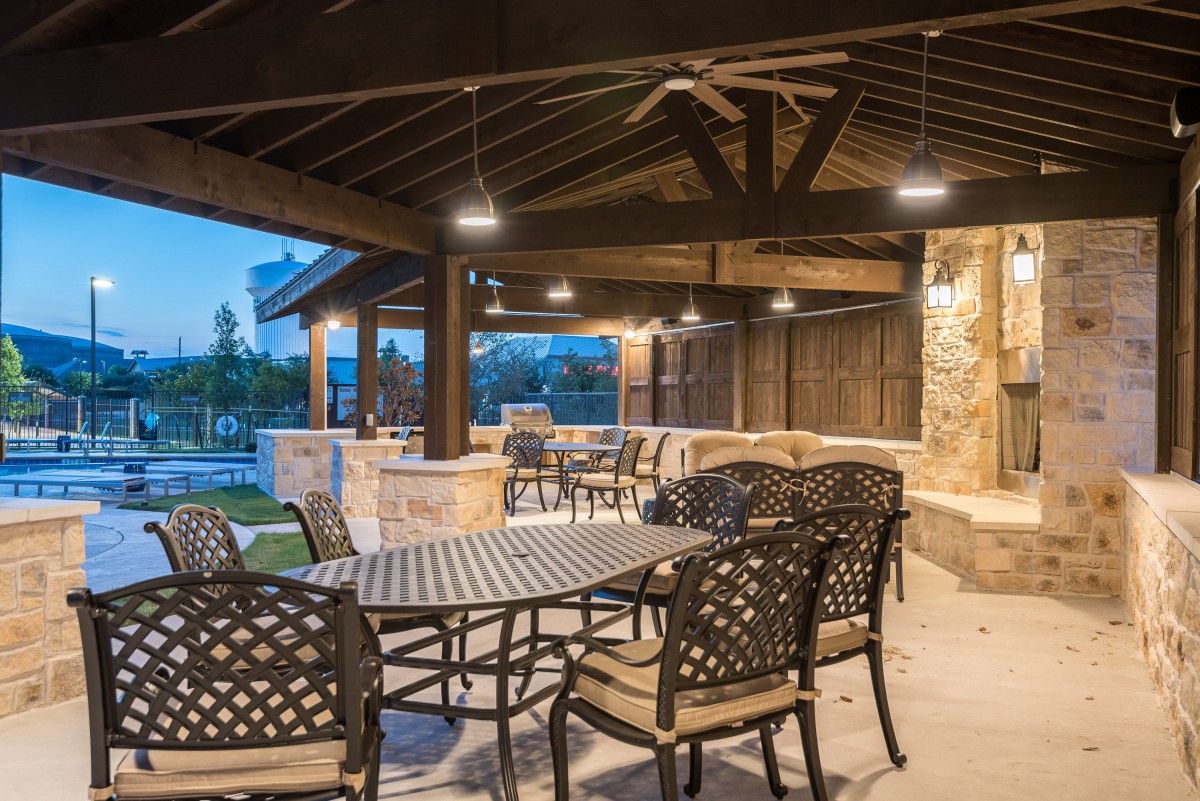 A beautifully designed outdoor patio with dining furniture under a covered structure, illuminated in the evening.