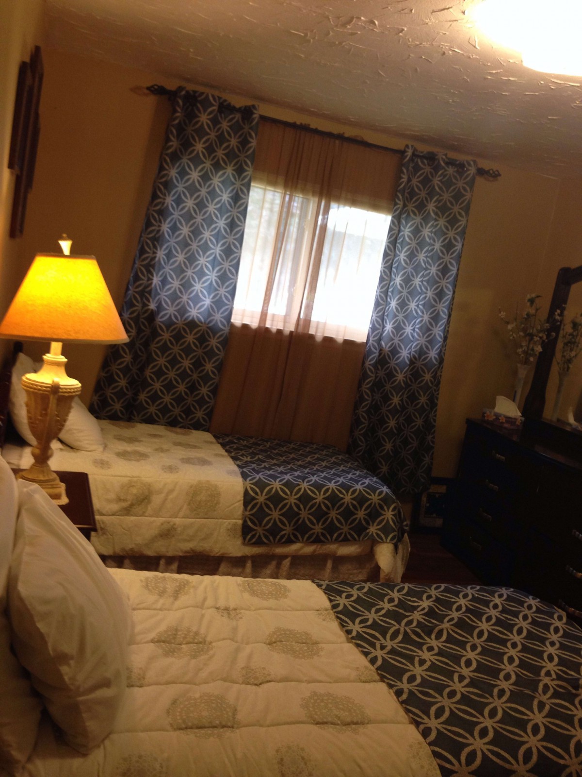 A cozy bedroom with two twin beds, illuminated by a bedside lamp and decorated with matching curtains.