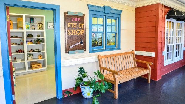 A cozy entrance to a fix-it shop with a wooden bench and potted plants.