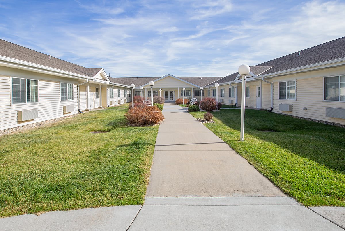 A pathway leading to a residential building, surrounded by lawns and under a clear sky.