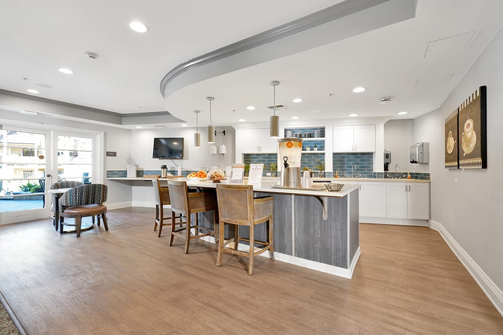 A modern kitchen with an island and bar stools, featuring wood flooring and pendant lighting.