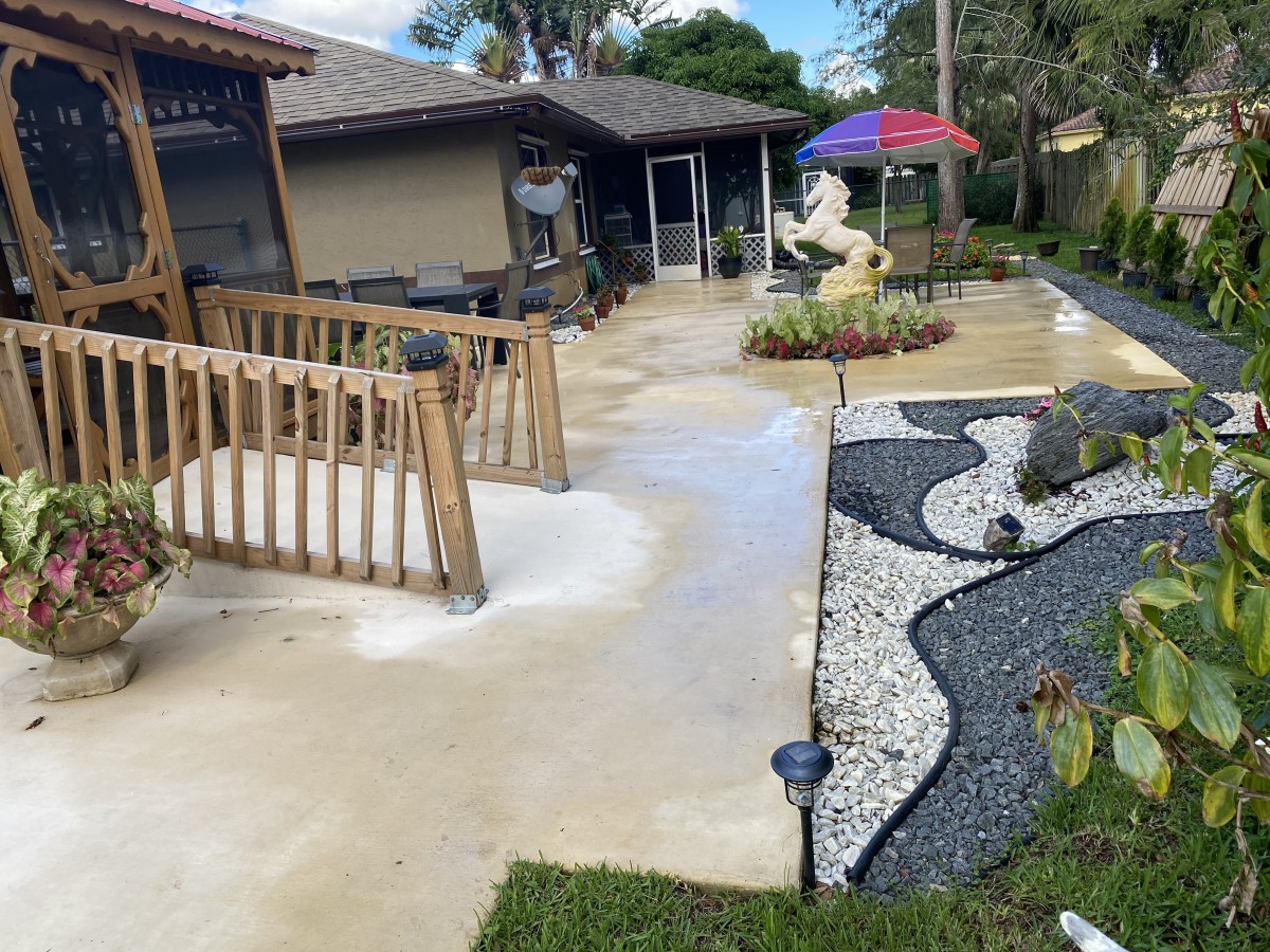 A well-maintained patio with a ramp, decorative pebble landscaping, and outdoor furniture under an umbrella.