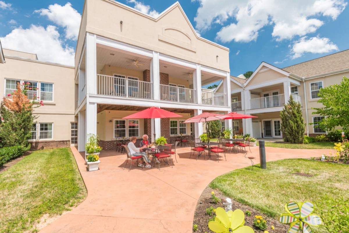 A sunny day at a building with a spacious patio, featuring red umbrellas and outdoor furniture.