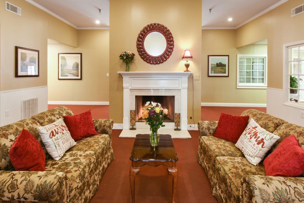 A cozy living room with a central fireplace, featuring two patterned sofas and a decorative mirror above the mantelpiece.