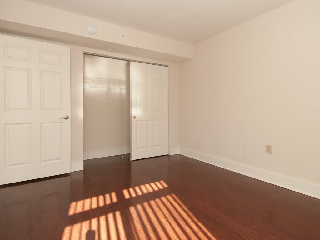 An empty room with wooden floors and sunlight streaming through the window, highlighting the closet with sliding doors.