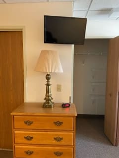 A small room with a dresser topped by a lamp and a television mounted above.