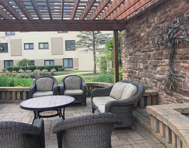A cozy outdoor seating area under a pergola with rattan chairs and a stone wall backdrop.