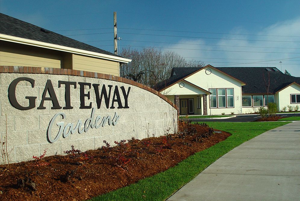 An entrance sign for Gateway Gardens with landscaped surroundings and adjacent buildings.