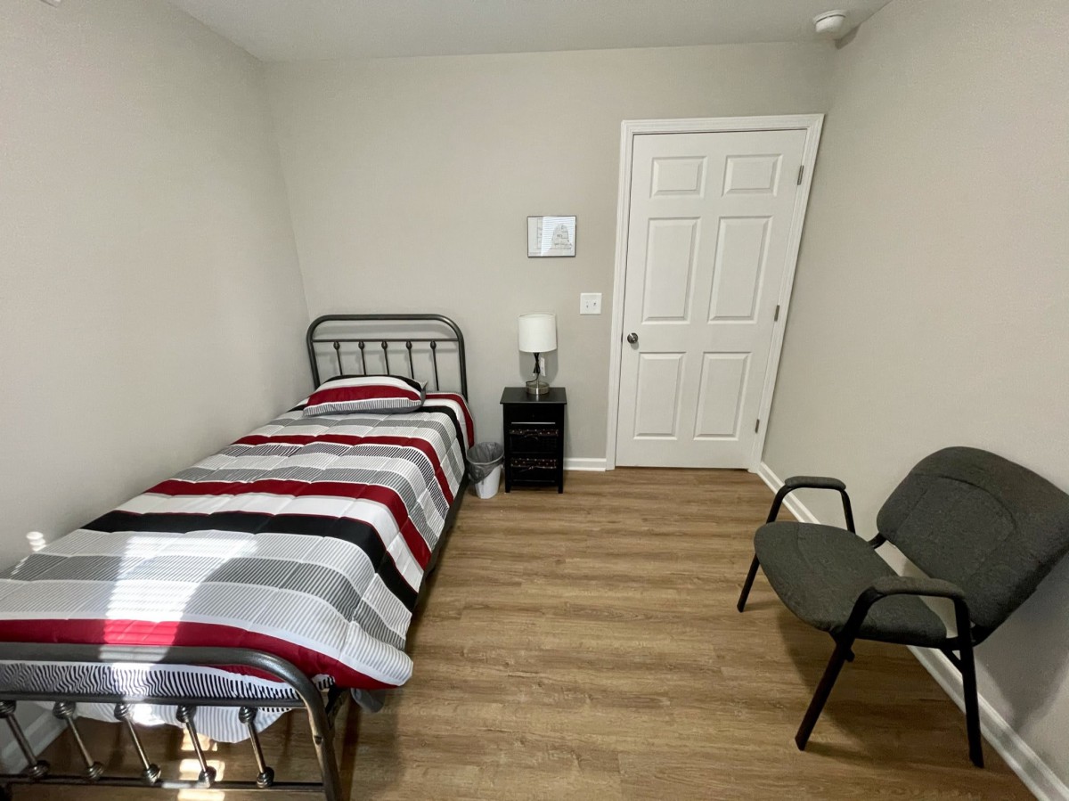 A minimalist bedroom with a single bed, striped bedding, and a nightstand featuring a lamp.