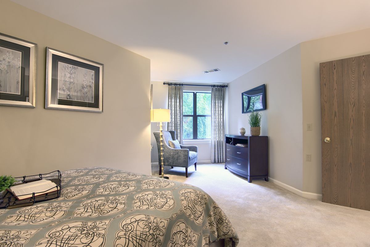 A modern bedroom with stylish decor, featuring a bed, armchair, and a large window providing natural light.