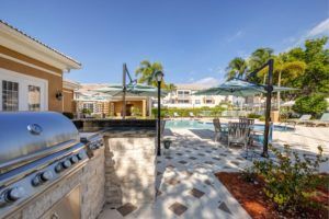 A sunny outdoor patio area with a pool, palm trees, and a grill for relaxation.