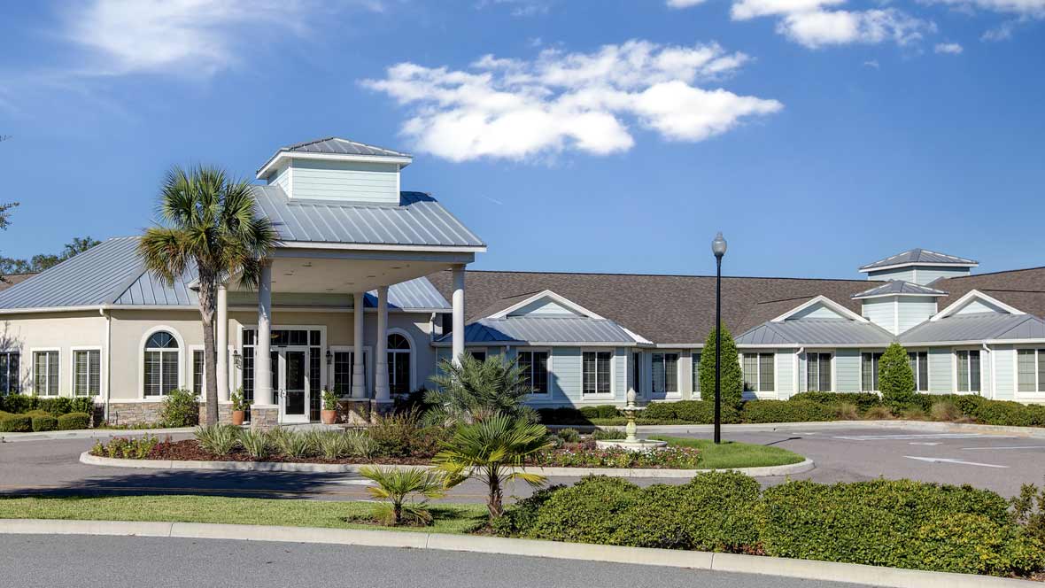 A large building with landscaped surroundings under a blue sky with clouds.