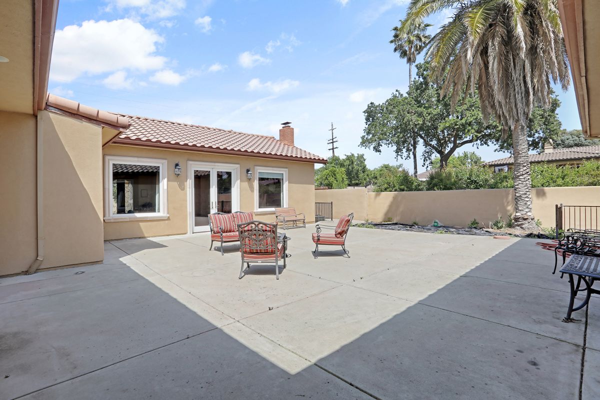 A spacious outdoor patio area with seating and a view of a well-kept yard featuring a palm tree.