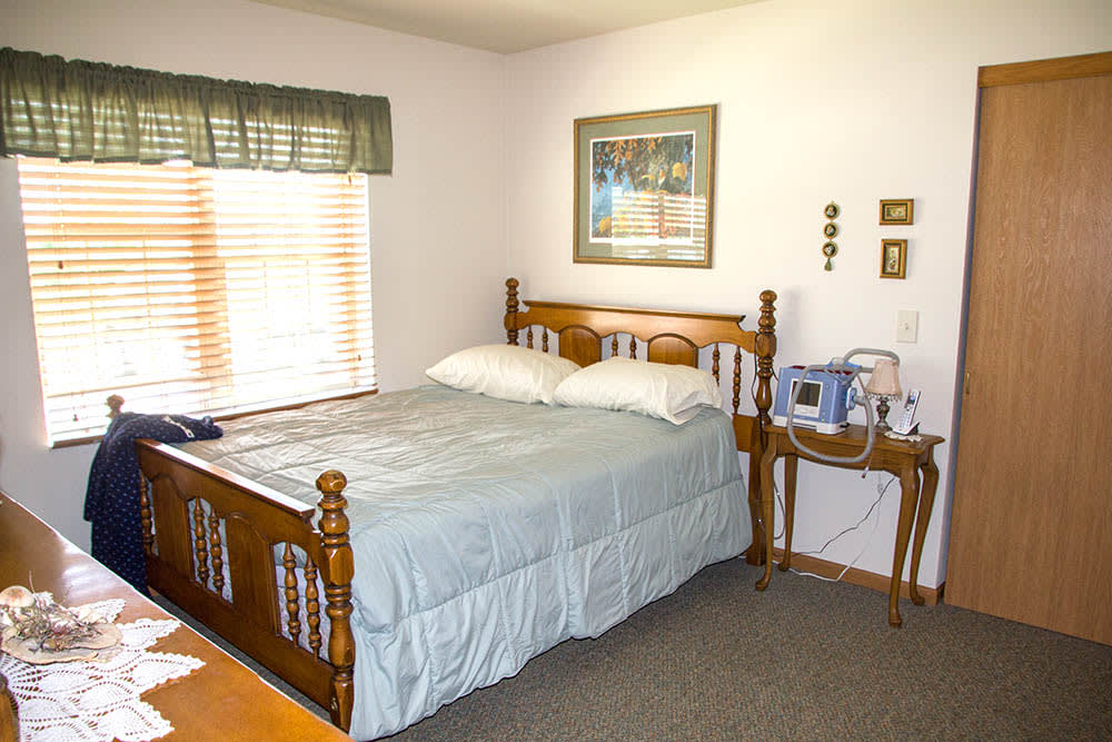 A cozy bedroom with a wooden bed, nightstand, and window with blinds.