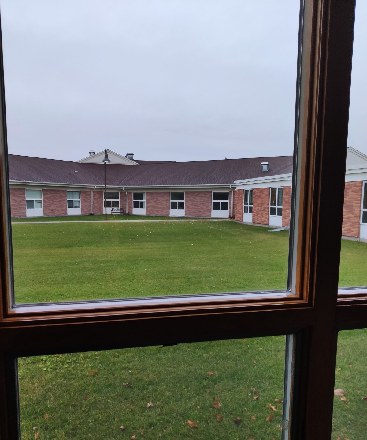 View through a window overlooking a grassy courtyard surrounded by a brick building.