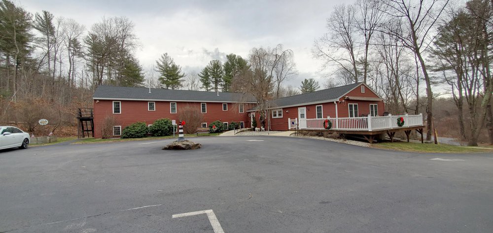 A red brick building with a parking lot in the foreground, surrounded by trees on an overcast day.